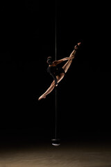 Beautiful young pole dancer woman on pylon isolated on black background.