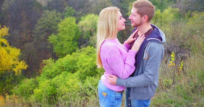 Happy couple on walk in autumn forest. Young girl kisses her boyfriend, looks happy right into camera. Caucasians couple cuddles on graft. High quality 4k footage