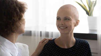 Close up caring doctor touching smiling hairless woman shoulder, congratulating with successful...