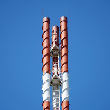 Three tall pipes made of iron, with a ladder and lightning protectors against a blue sky.