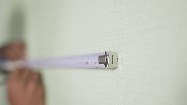 Close up of hands, Man holding pen and measuring tape while marking or drawing line on wall - Concet of home improvement and renovation
