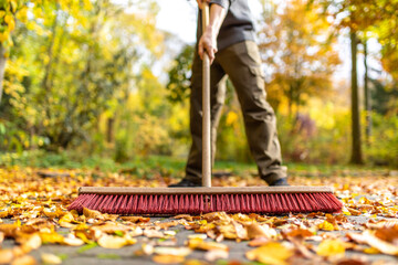 Mit großem Besen Blätter im Herbst zusammen fegen