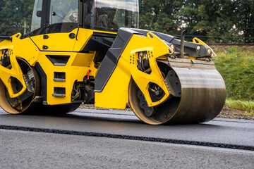 Fototapeta na wymiar Asphalt road roller with heavy vibration roller compactor press new hot asphalt on the roadway on a road construction site. Heavy Vibration roller at asphalt pavement working. Repairing.