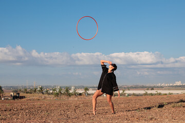 Female flow artist waiting to catch her Hula hoop after throwing it high in the air. Wide shot in natural morning sunlight.  © Calacuda_stock