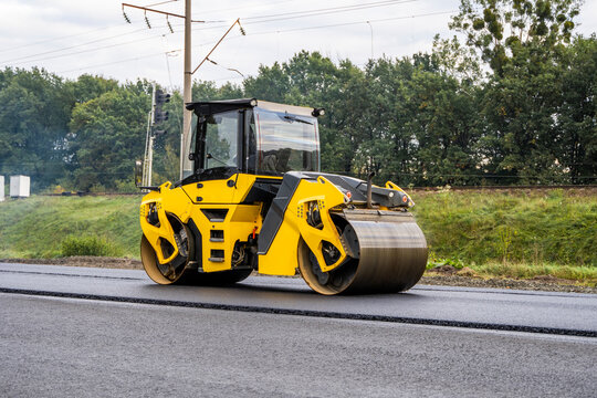 Asphalt road roller with heavy vibration roller compactor press new hot asphalt on the roadway on a road construction site. Heavy Vibration roller at asphalt pavement working. Repairing.