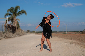Young Middle Eastern woman in a dance pose with a Hula hoop. Wide shot in natural morning sunlight. 