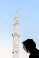 Fototapeta na wymiar Silhouette of muslim arabic woman, covered in black abaya in front of spile top of white Grand mosque, Abu Dhabi, UAE, evening magrib pray time