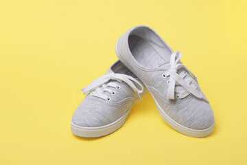 Pair of grey sneakers with tied shoelaces on yellow background