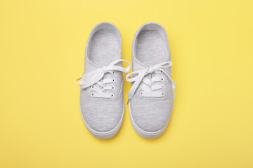 Pair of grey sneakers with tied shoelaces on yellow background.
