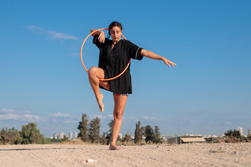 Female flow artist dancing with a Hula hoop outdoors, with one leg on the ground. Wide shot in natural morning sunlight.  © Calacuda_stock