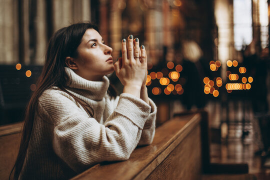 a young pretty woman came to the temple to pray to God. The parishioner of the church sits on a bench with her hands folded for prayer and heartily prays. copy space