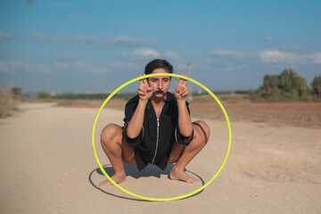 Young Middle Eastern woman in a dance pose with a Hula hoop. Wide shot in natural morning sunlight.  © Calacuda_stock
