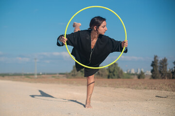 Female flow artist dancing with a Hula hoop outdoors, with one leg on the ground. Wide shot in natural morning sunlight.  © Calacuda_stock