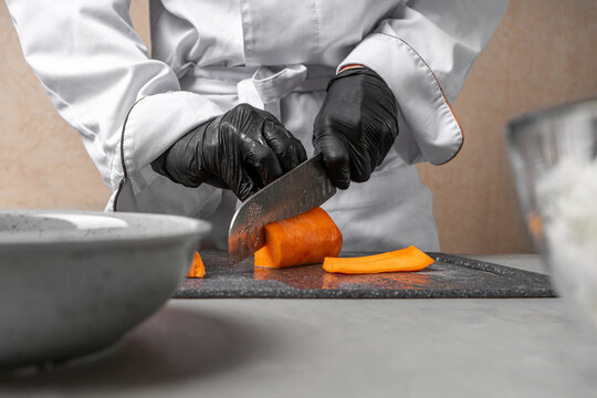 The chef cuts the carrot on the grey Board.