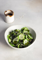bowl with wakame seaweed cucumber salad on gray background. Traditional Japanese Sunomono salad. Vertical image