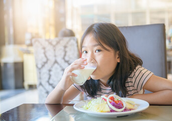 Asian little cute girl is drinking a glass of milk and eating salad
