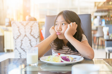 asian child girl with expression of disgust against vegetables in restaurant,