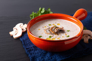 Food concept organic mushroom cream soup in orange ceramic handle bowl on black slate stone with copy space
