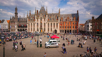 Fototapeta premium Bruges, Belgium - May 12, 2018: Tourists And Locals Walk On A Sunny Day On Main Square