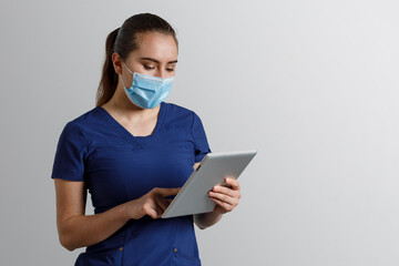 Mujer latina, con uniforme de enfermera usando cubrebocas y careta, sosteniendo una tableta digital en las manos, y un fondo color gris con espacio para texto