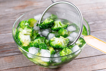 Blanched broccoli cabbage cooling down in icy water in a bowl on table