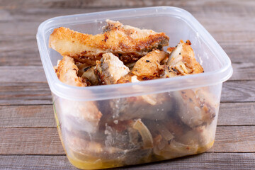 Homemade fried fish in a container on a wooden table