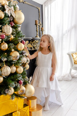 A cute blonde girl decorates a tree before Christmas at home. Happy childhood. Decorating a Christmas tree before Christmas.