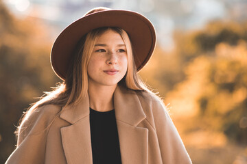 Smiling teen girl 12-13 year old wearing stylish hat and beige jacket over yellow nature close up....