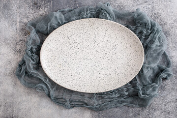Empty oval plate with gauze tablecloth on concrete background. Top view, with copy space