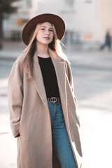 Teenage girl 14-15 year old wearing casual hat and winter coat in city street outdoors. Looking at camera. Teenagerhood.