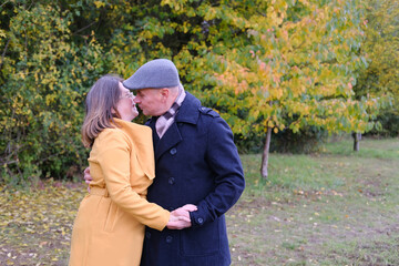 middle-aged man and woman in coats are walking in the autumn park against the background of trees, the concept of a healthy lifestyle, good mood, happiness at any age