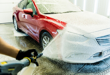Worker washing car with active foam on a car wash.