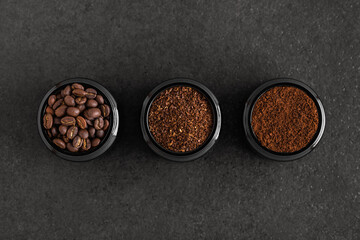 Whole roasted coffee beans and ground coffee powder in three different jars on black textured...