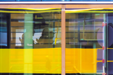 Abstract blurred background of city life: reflection in the window glass of a yellow city bus with passengers