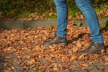 Close up view of woman walking on fallen orange leaves lying on paving stones of avenue in public park. Selective focus. Abstract autumn background.