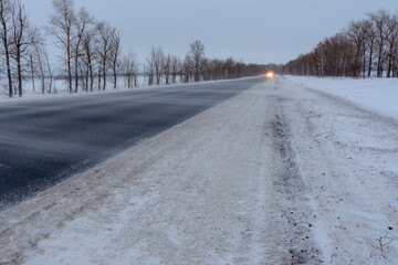 Snowstorm on the highway. Patterns on the winter highway in the form of four straight lines. Snowy road on the background of snow-covered forest.