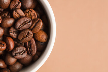Coffee beans, with ground (selective focus on coffee beans) and white ceramic cup, brown background.