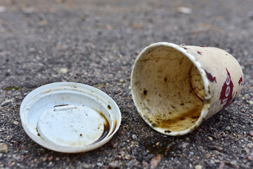 Crumpled a paper coffee cup on asphalt. Discarded disposable coffee cup with a plastic lid on road....