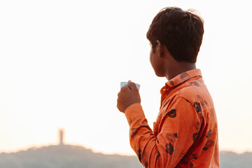 Portrait of an Indian kid holding coffee cup looking at the sunrise