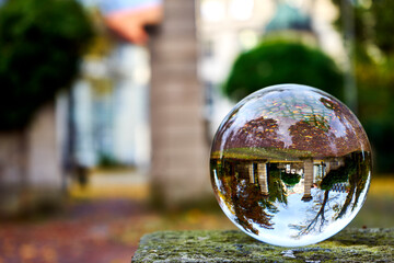 View through the crystal ball to an entrance gate with trees in the surroundings, ball on a stone plate, blurred background