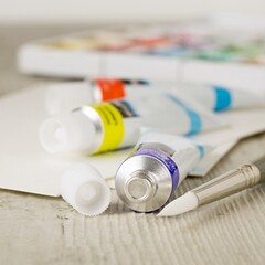 A close up of an artists paintbrush with tubes of paint and supplies on a wooden table