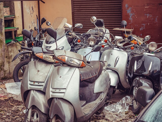 Several mopeds stand in a littered place waiting for repairs