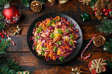 Obraz na płótnie Canvas Christmas Red Cabbage, carrots, apples and pecan nuts Salad with decoration, gifts, green tree branch on wooden rustic table