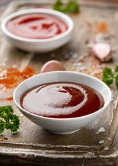 Barbecue sauce in white bowl on wooden board with herbs