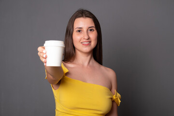 Beautiful young woman holding a paper cup with place for text. Disposable cup for coffee or tea with a blank space for text in the hands of women.