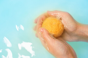 Orange bubbling ball of bath salt in the hands on blue water background. Bomb for the bath it...