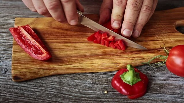male slicing  red peper on wooden chopping board very close up view