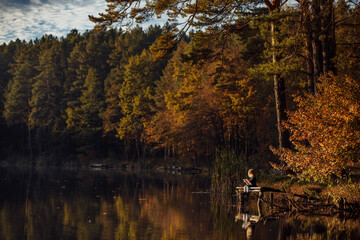 girl reads a book in autumn by the river. lonely young woman reads a book on a wooden bridge