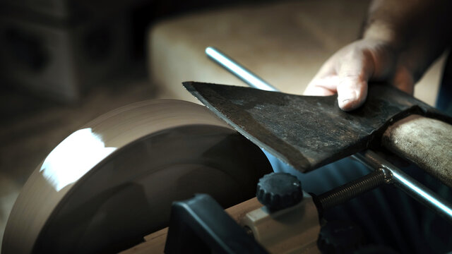 Asian man sharpening axe on a grinder