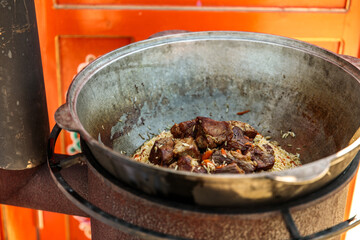 real Uzbek pilaf in a cauldron. Carrots and meat in a cauldron with rice on a live fire in a huge cauldron for pilaf. Cooking Uzbek festive pilaf
